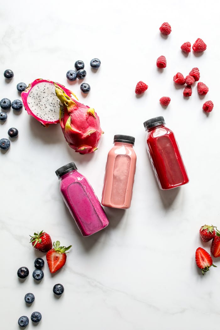 Colorful fruit smoothies with dragon fruit, berries, and more on a white background.
